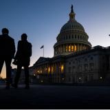 People waling in front of the US Capitol building at sunset. 