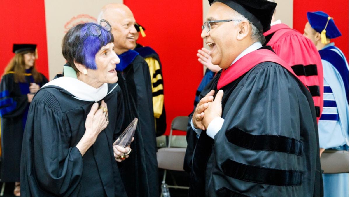 Representative Rosa DeLauro in her regalia speaking to a professor at a university graduation.