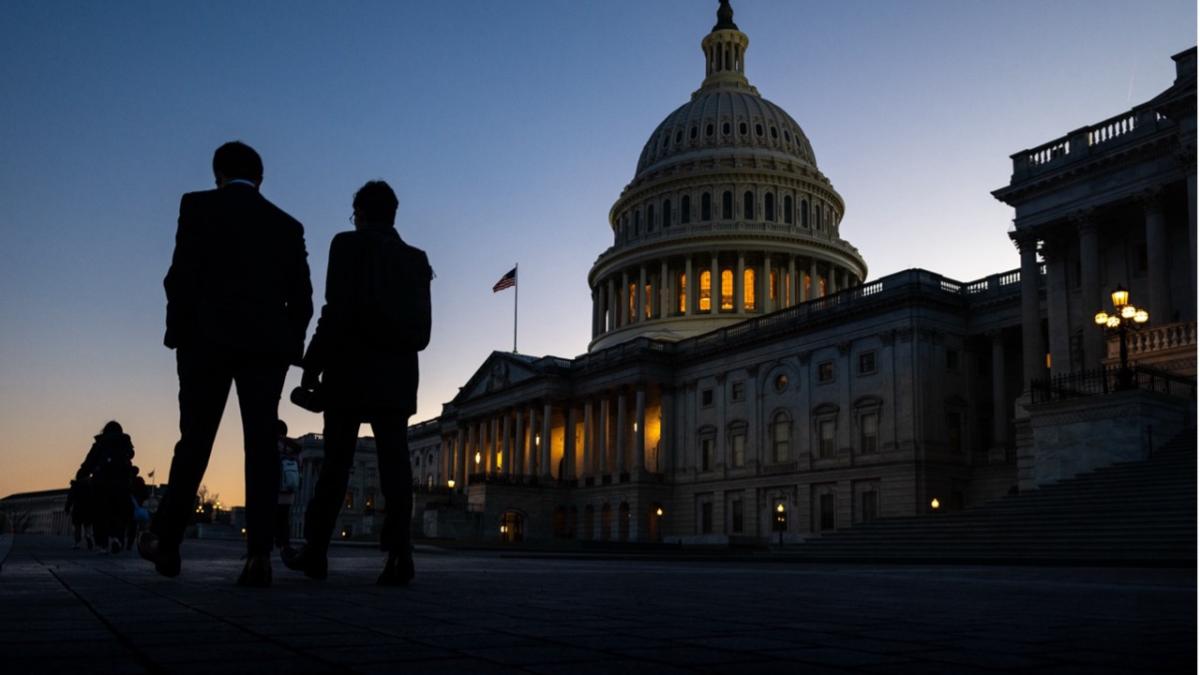 People waling in front of the US Capitol building at sunset. 